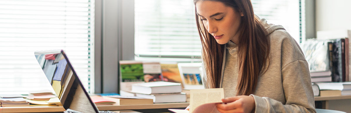 A high school student working independently at her desk with a book and laptop.